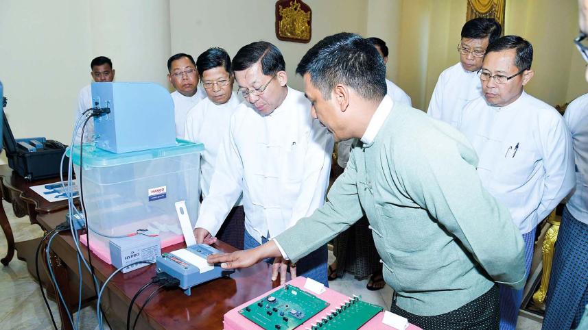 মিয়ানমারের নির্বাচন কমিশনের সদস্যরা মিন অং হ্লাইংকে ইভিএম দেখাচ্ছেন। ফাইল ছবি: এএফপি